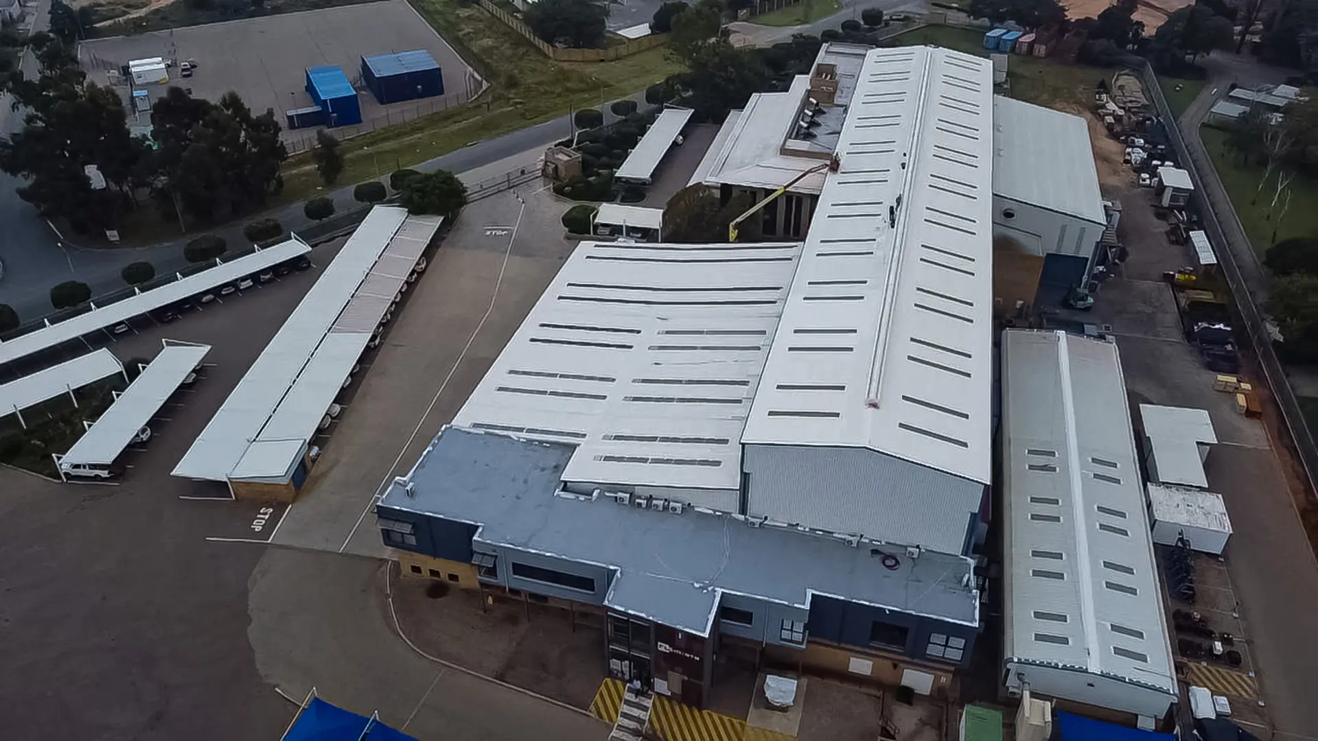 Aerial view of expansive commercial and industrial buildings with white roofs and shaded parking, ideal for local roof contractors near me.